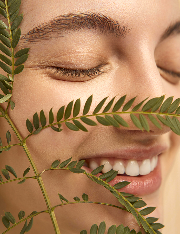 Mujer en primer plano sonriendo detrás de una planta