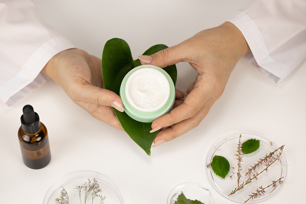 Close-up,Hands,Hold,Cosmetic,Jar,With,Cream,On,Fresh,Green